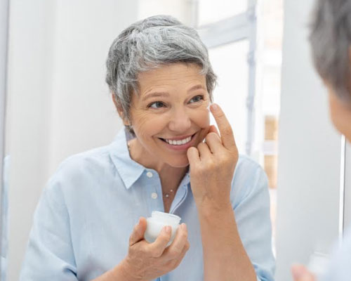 Eyelid cancer prevention, smiling woman looking in mirror, about to apply sunblock to face