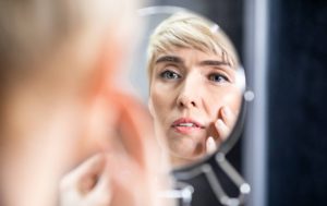 Woman examining her face in the mirror looking for changes from aging.