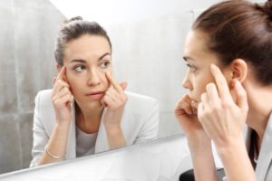 Woman checking herself in the mirror for her face that might look aged.