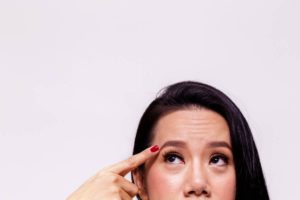Woman pointing to her eyebrows wondering what ages her forehead.