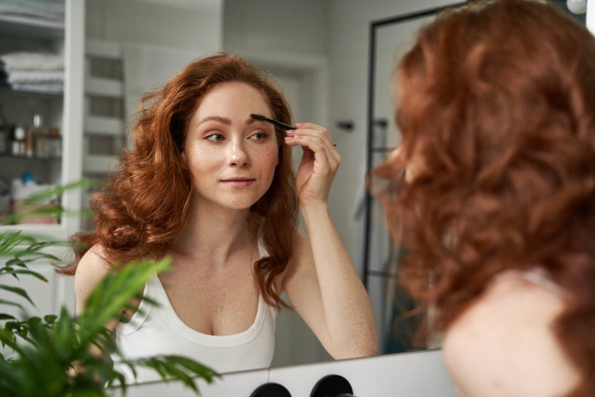 Woman brushing her eyebrows while looking in the mirror.